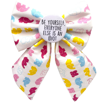 Dog bow tie - Sailor bow themed. White Bow, with pink, yellow, white and blue cartoon elephants all over. Has slogan "Be yourself, everyone else is an idiot" on a badge in the middle of the bow.