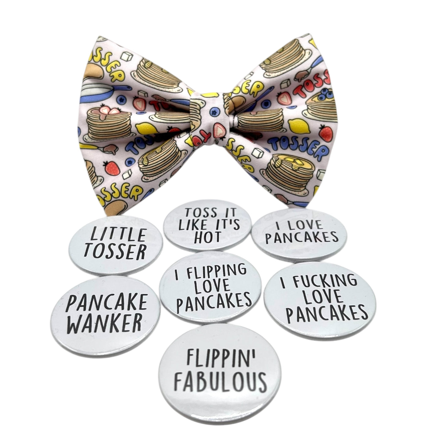 Pancake Day themed bow tie for pets. Light purple fabric bow with pancakes on it, with text " TOSSER" in red, yellow and blue. Showing 7 different badge options