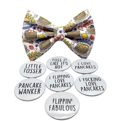 Pancake Day themed bow tie for pets. Light purple fabric bow with pancakes on it, with text " TOSSER" in red, yellow and blue. Showing 7 different badge options