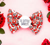 Dog bow tie. White colour with red sauce sachets with a little saucy written on them. The bow tie has a badge in the middle with "A little Saucy" wriiten on  it.