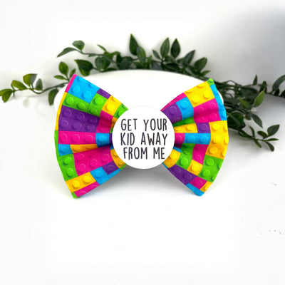 Lego block theme bow tie. Very colourful. Purple, pink, yellow, blue and Green. With a badge in the centre. 