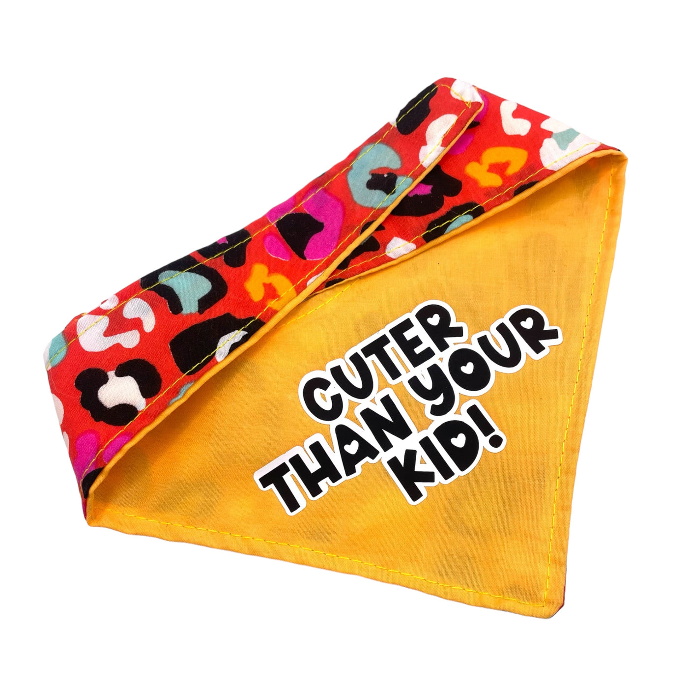 Reversible pet bandana. Multi colour animal print onside. Colours are red, black, blue, black and pink. On the reverse side - this is orange with the text "Cuter than your kid" in bold, black text, with a white edging. 