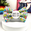 A novelty dog bow tie, with colourful beach balls pattern on a blue background. Badge in middle that says “sun’s out balls out” 