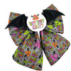 A Halloween themed dog bow featuring a grey fabric printed with colourful cartoon poop emojis, pumpkins, bats, and the text 'BAT SHIT CRAZY' in neon colours, with black bat-wing tips and a white circular centre sticker.