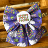 A purple Halloween dog bow with a white centre badge reading 'Spooky Little Fucker' in multicoloured letters. The bow fabric has a Halloween print with white ghosts, green zombies, tombstones, stars, and the phrase 'You're So Little Fucker' repeated in colourful text.