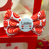Red and white dog bow tie with heart pattern and 'Ladies Man' button on a red box.